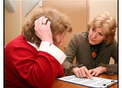 Two women are sitting at a table. One is explaining a document to the other. 