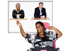 A woman in a black and white shirt seated in a wheelchair is pointing to a poster. The poster has a picture of a man and a woman on it. The woman is pointing choosing the woman.