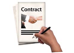 An image of a hand holding a pen signing a contract. On the front of the contract is two hands shaking in agreement.
