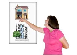 A young woman with a disability in a pink t shirt is standing in front of images of two buildings.  One is a house, the other is a block of units. she is pointing at the block of units, she is choosing.