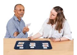 A man in a blue shirt is holding a card he chose from a group of cards in front of him. He is showing a woman beside him.