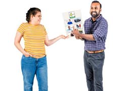 A young woman in jeans and a yellow t shirt is jointly holding a document, it has picture on it. The man beside her is smiling and is pointing to the pictures.