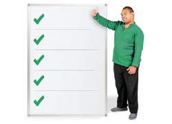 A man standing beside a checklist. the checklist has five ticks on it, The man is in a green shirt and jeans, he is holding his thumb up.