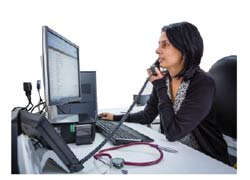 A female doctor is seated at her desk in front of a computer. She is talking on the phone.