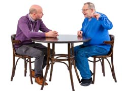 Two men sitting at a table. One is listening to the other.