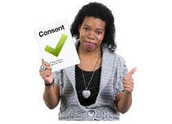 A woman with a great jumper on is holding a card that says consent. She is holding her thumb up.