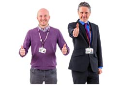 Two men, one is a purple jumper, the other in a suit. They both have their thumbs up in agreement.